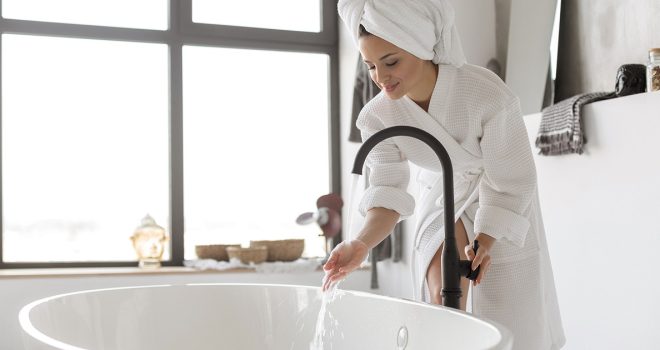 Nainen laskee lämmintä kylpyvettä, jota lämminvesivaraaja säilyttää.